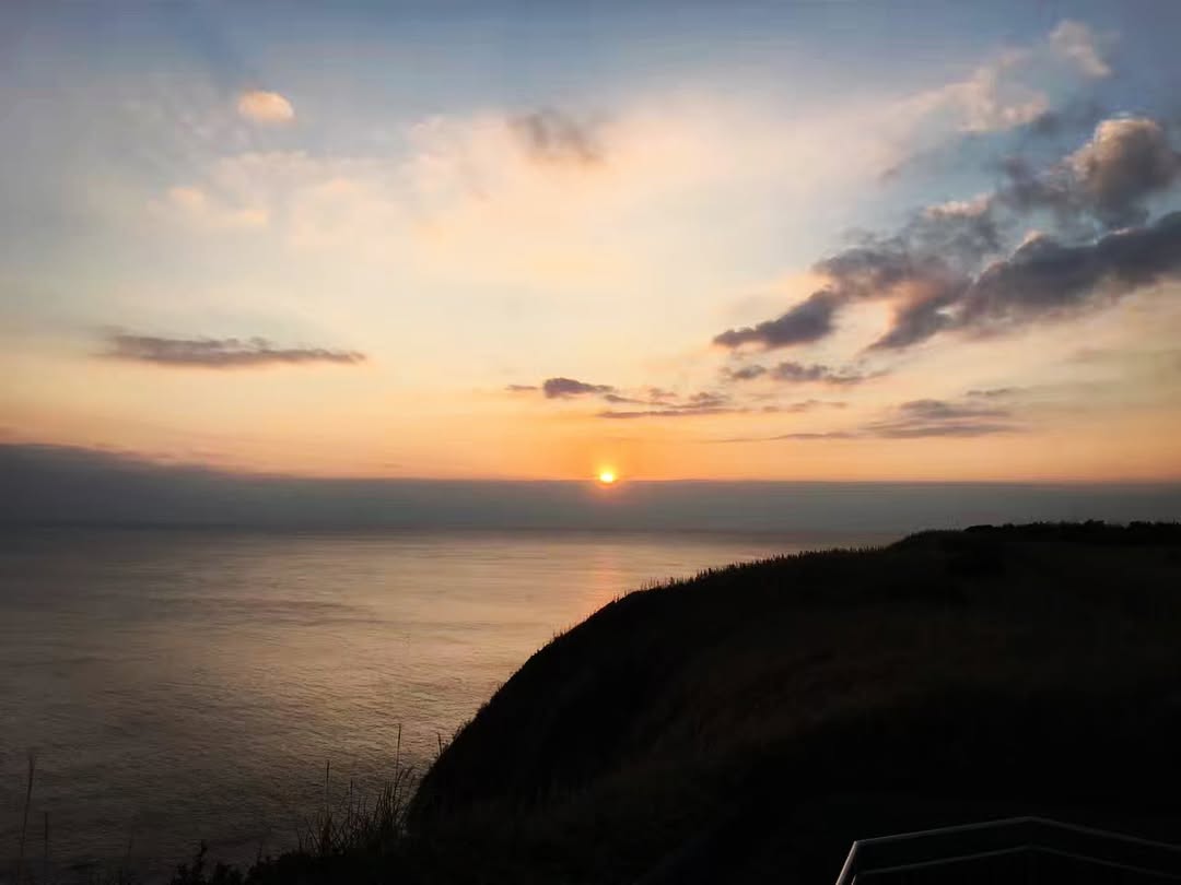 夕陽沉向海面，近處山崖已隱入暮色